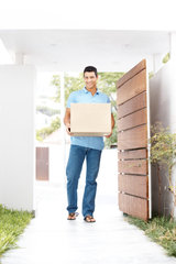 Happy young man walking in his new apartment with a cardboard box
