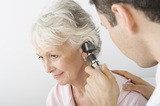 Mature male doctor examining patient's ear using otoscope in clinic