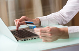 Man's hand entering data using laptop while holding a credit card in the other hand