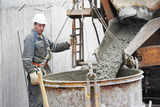 Builder worker pouring concrete from automobile mixer into construction barrel