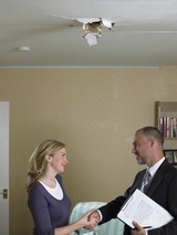 Mid adult woman shaking hands with mature man holding clipboard beneath hole in ceiling