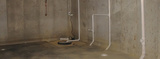 A poured concrete basement of a newly constructed house showing the sump pump in the corner.