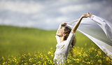 Young happy woman standing in yellow rapeseed field holding a white piece of cloth in the wind expressing freedom.