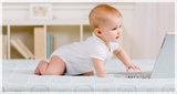 Side view of curious baby crawling in bed toward laptop