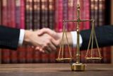 50278233 - justice scale on wooden table with judge and client shaking hands in background at courtroom