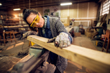 Portrait view of happy attractive hardworking middle aged professional female carpenter worker looking and choosing wood in the workshop or garage. (Portrait view of happy attractive hardworking middle aged professional female carpenter worker looking