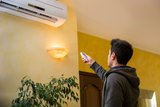 Young man switching on or adjusting the wall mounted air conditioner in the living room with a remote control
